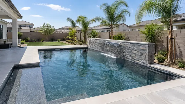 Newer Gilbert, Arizona backyard in a master-planned community: a modern rectangular pool with dark gray pebble finish, a sheer descent water feature on a stacked-stone wall, porcelain deck and young palms