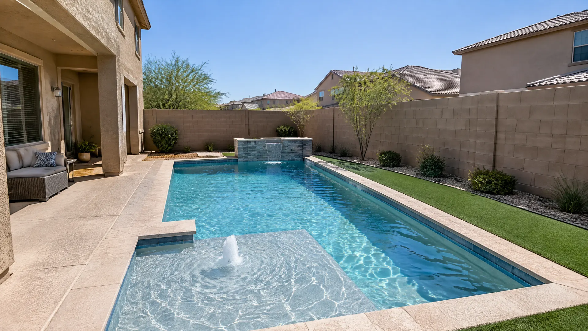 Compact backyard behind a two-story Gilbert, Arizona home from the late 2000s: a small geometric pool with a sun shelf and bubbler, narrow deck, artificial turf strip and a block wall with neighbors' rooftops visible