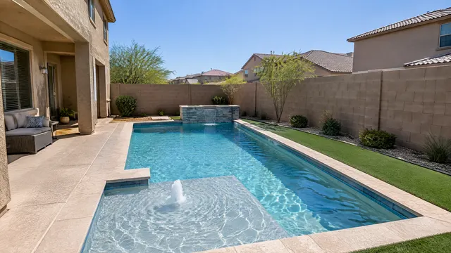 Compact backyard behind a two-story Gilbert, Arizona home from the late 2000s: a small geometric pool with a sun shelf and bubbler, narrow deck, artificial turf strip and a block wall with neighbors' rooftops visible