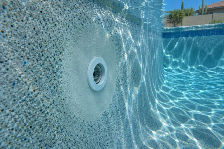 Freshly patched return fitting on a pool wall under clear water, smooth repair compound blending into the plaster
