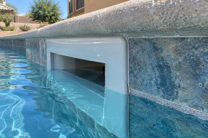 Pool skimmer throat at the waterline showing a hairline crack where it meets the pool wall tile, close view
