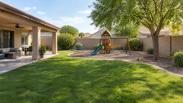 Backyard in Gilbert, Arizona where an old pool has been filled in and finished: new green lawn and a small play area where the pool used to be, covered patio, block wall and a shade tree, afternoon light