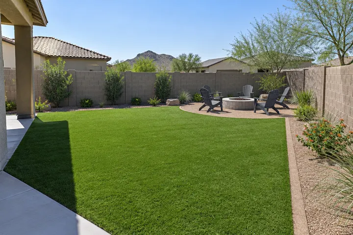 Finished backyard where a pool was removed: new artificial turf, a fire pit with chairs and decomposed granite borders by a block wall